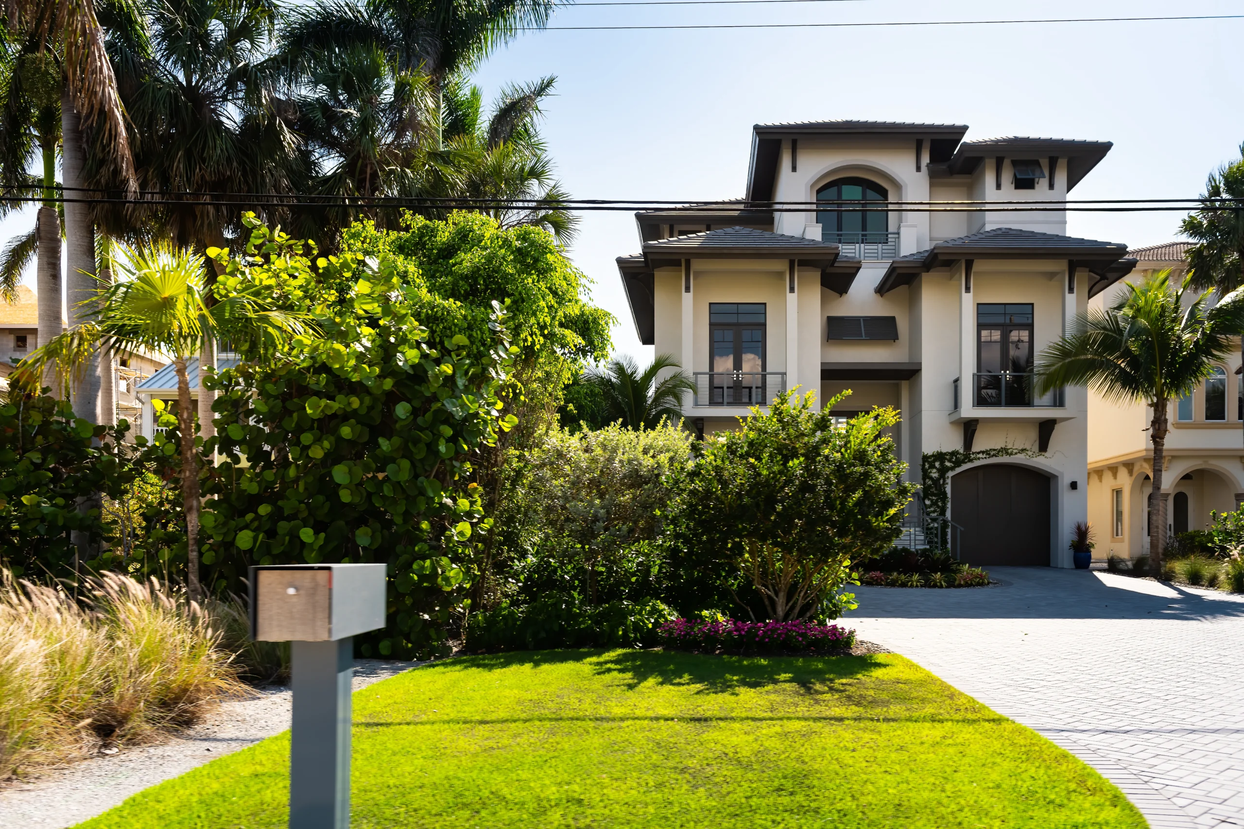 Single-story house with a two-car garage, neatly trimmed lawn, small palm trees, and a "For Rent" sign in the front yard beneath a clear blue sky—ideal for those seeking Homes for Rent in Naples.