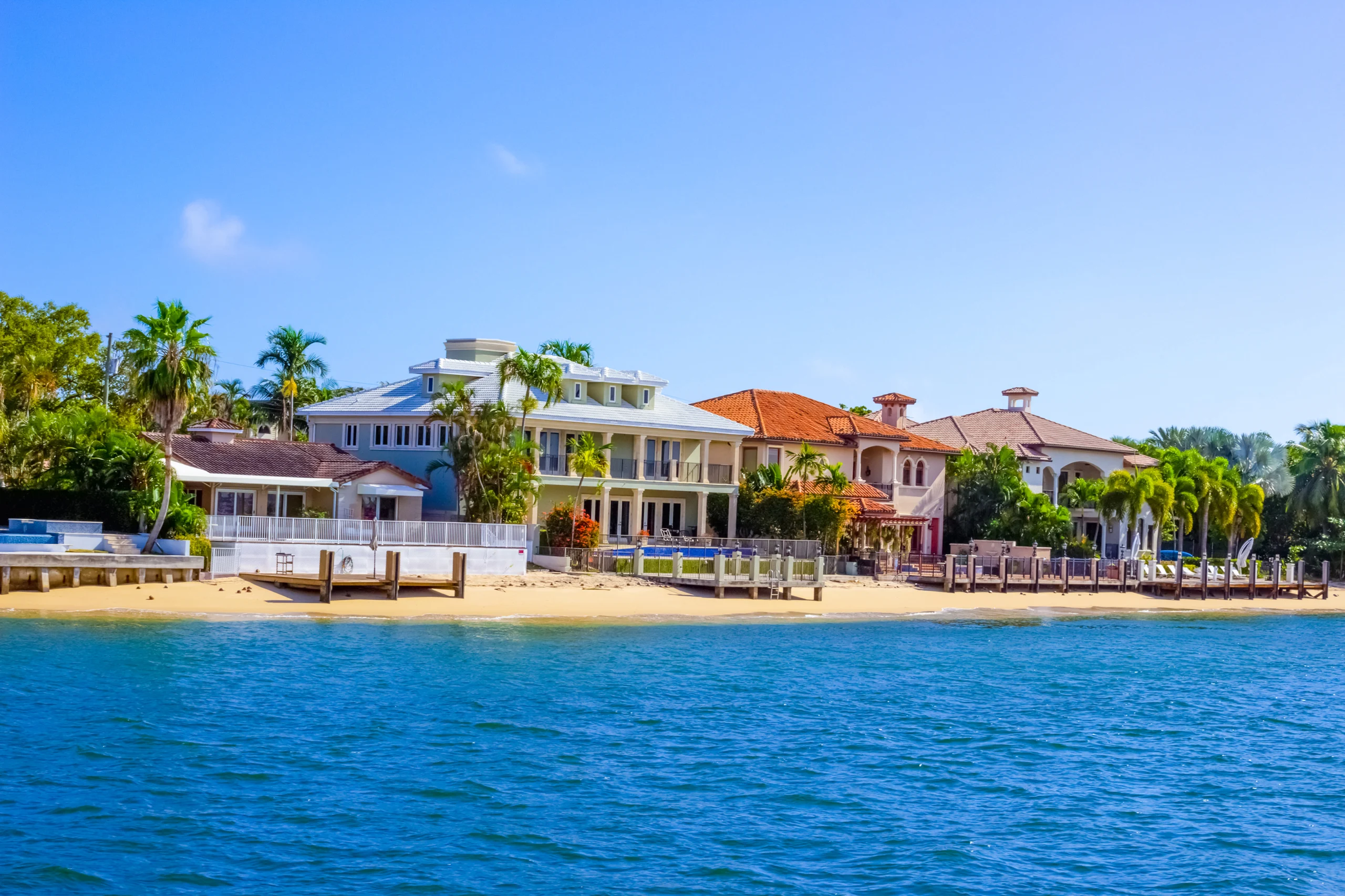 Single-story house with a two-car garage, neatly trimmed lawn, small palm trees, and a "For Rent" sign in the front yard beneath a clear blue sky—ideal for those seeking Homes for Rent in Naples.