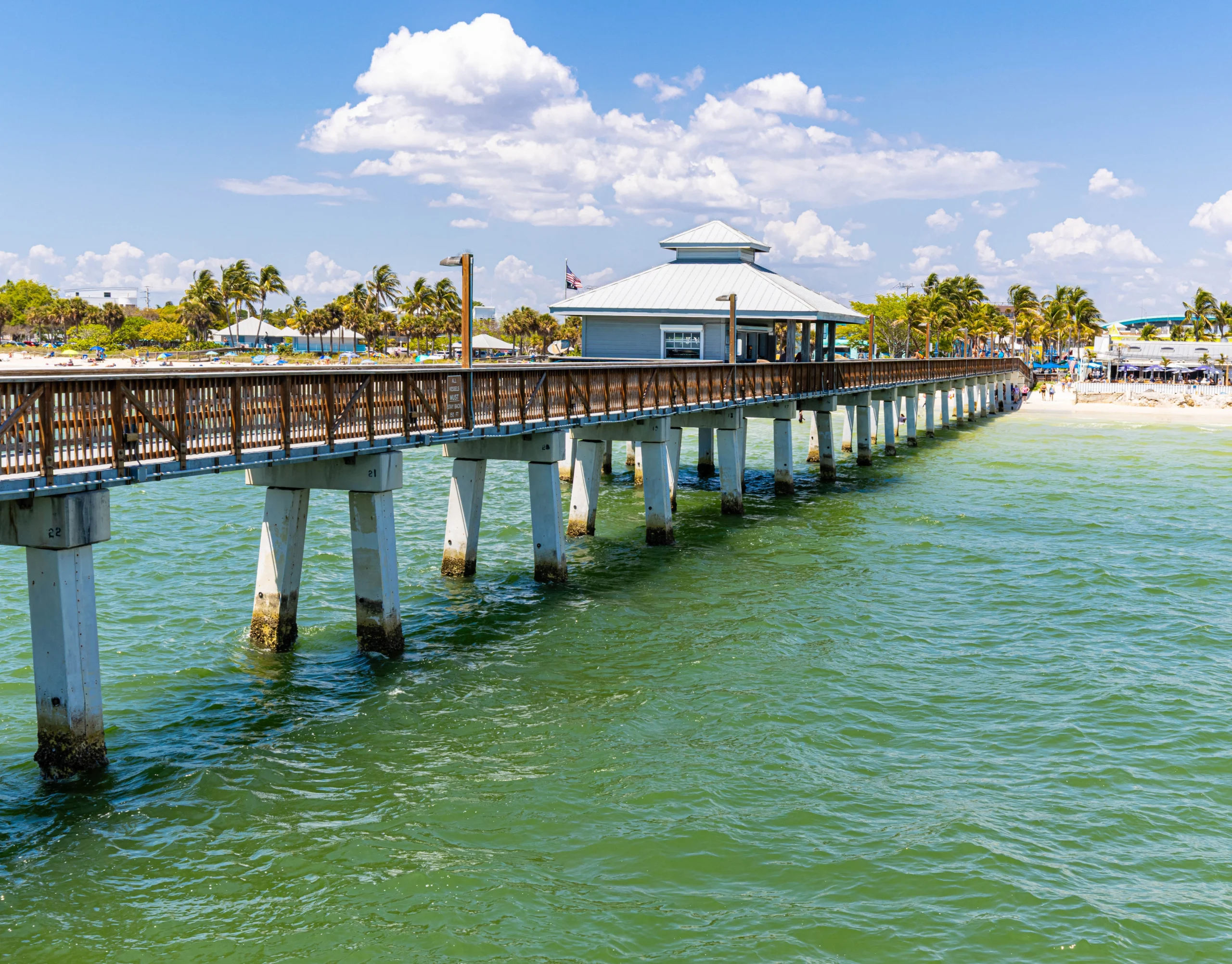 Single-story house with a two-car garage, neatly trimmed lawn, small palm trees, and a "For Rent" sign in the front yard beneath a clear blue sky—ideal for those seeking Homes for Rent in Naples.