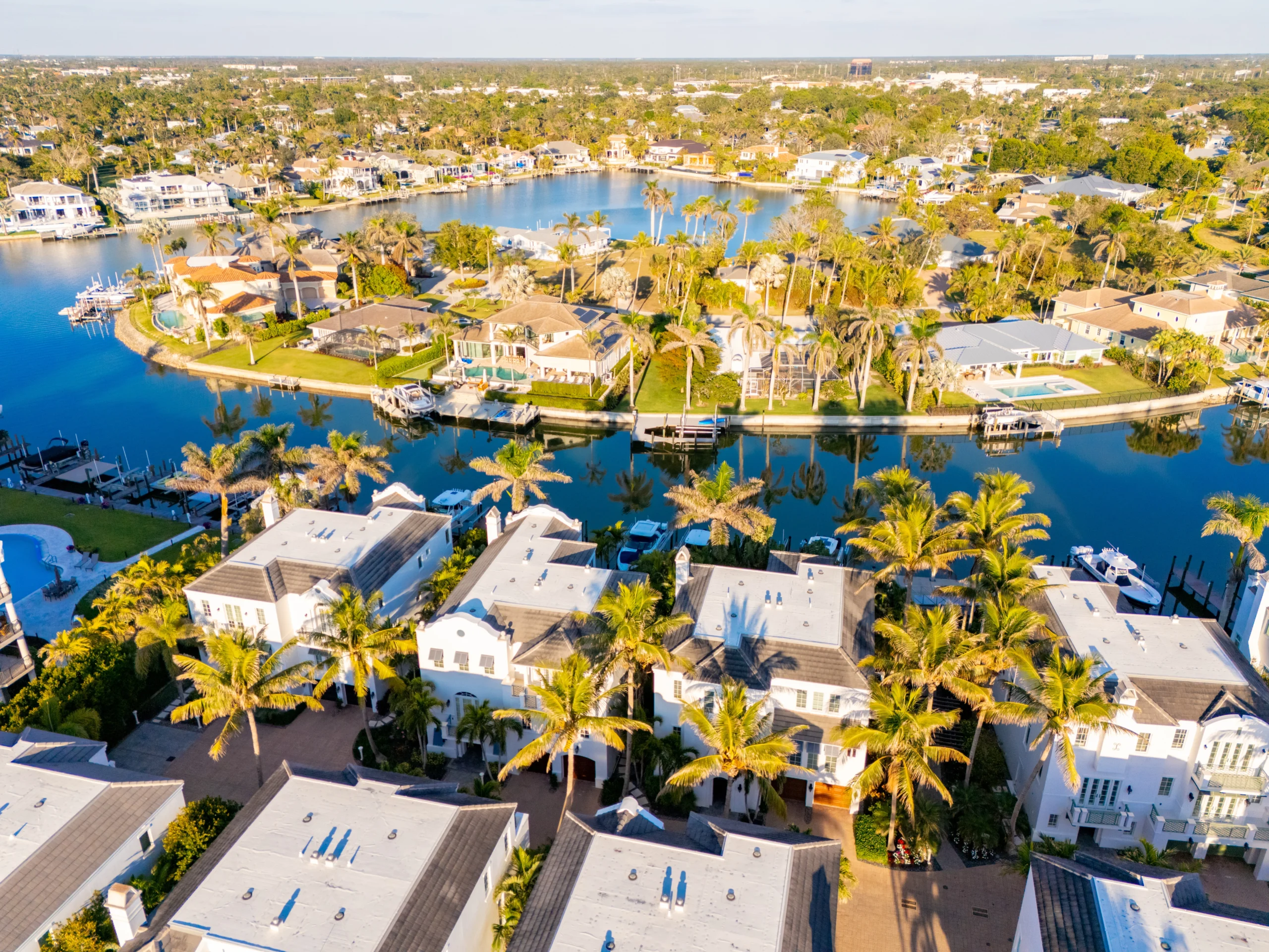 Single-story house with a two-car garage, neatly trimmed lawn, small palm trees, and a "For Rent" sign in the front yard beneath a clear blue sky—ideal for those seeking Homes for Rent in Naples.
